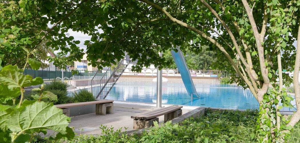 Schwimmbecken mit Sprungturm, Blick durch viel Grün